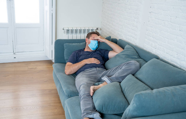 Sad man with protective face mask at home living room couch feeling tired and worried suffering depression amid coronavirus lockdown and social distancing. Mental Health and isolation concept. - Photo, image