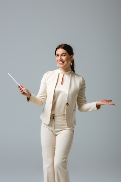 Mujer atractiva en ropa formal sonriendo a la cámara mientras sostiene la tableta digital aislada en gris, concepto de cuerpo positivo
  - Foto, Imagen