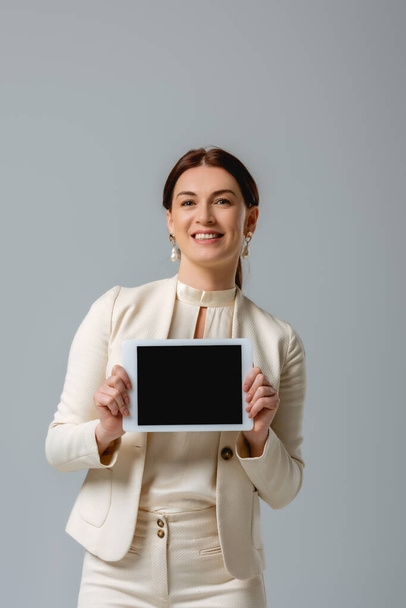 Attractive woman smiling at camera and showing digital tablet isolated on grey  - Valokuva, kuva