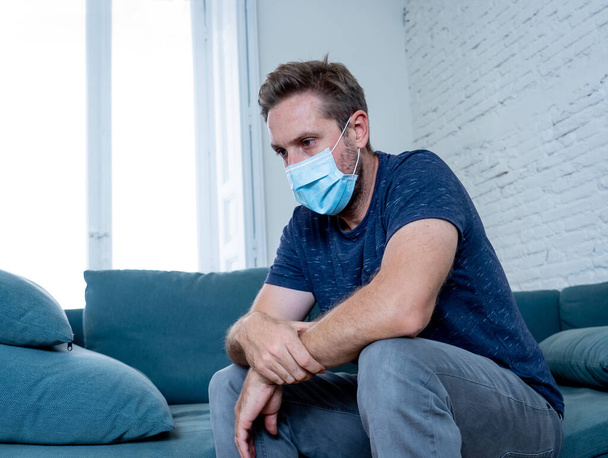 Sad man with protective face mask at home living room couch feeling tired and worried suffering depression amid coronavirus lockdown and social distancing. Mental Health and isolation concept. - Foto, Imagem