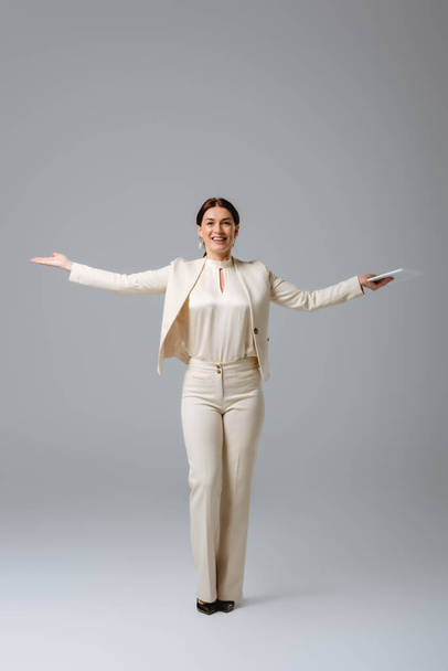 Positive businesswoman pointing with hand and holding digital tablet on grey background, concept of body positive  - Φωτογραφία, εικόνα