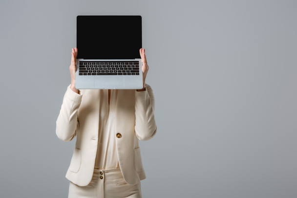 Mujer en ropa formal sosteniendo portátil con pantalla en blanco cerca de la cara aislada en gris
  - Foto, Imagen