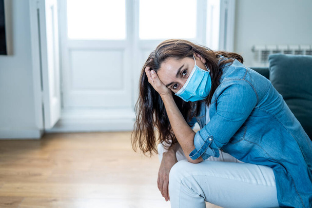 Sad latin woman with protective face mask at home living room couch feeling tired and worried suffering depression amid coronavirus lockdown and social distancing. Mental Health and isolation concept. - Foto, imagen