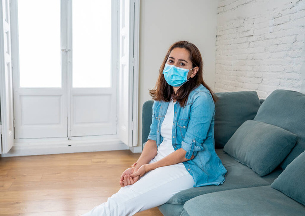 Sad latin woman with protective face mask at home living room couch feeling tired and worried suffering depression amid coronavirus lockdown and social distancing. Mental Health and isolation concept. - Foto, Imagem