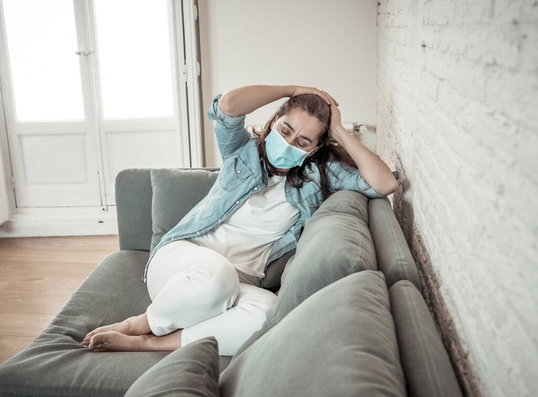 Sad latin woman with protective face mask at home living room couch feeling tired and worried suffering depression amid coronavirus lockdown and social distancing. Mental Health and isolation concept. - Foto, imagen