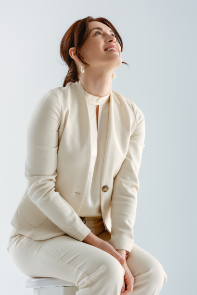Позитивная деловая женщина смотрит вверх, сидя на стуле изолированы на серый
  - Фото, изображение