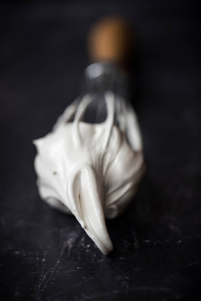 Hand ballon garde met geklopt ei wit meringue mix. Close-up op zwarte achtergrond. - Foto, afbeelding