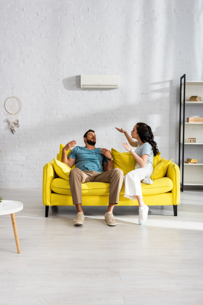 Mujer joven soplando en novio que sufre de calor en el sofá en la sala de estar
 - Foto, Imagen