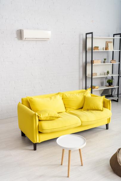 Interior del salón con sofá amarillo y aire acondicionado en la pared
 - Foto, Imagen