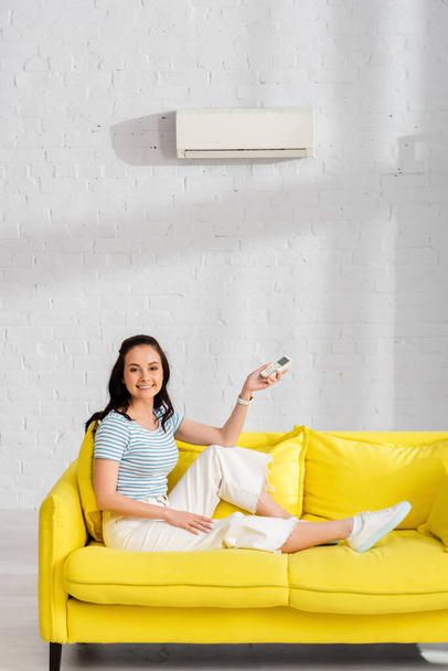 Atrakcyjna uśmiechnięta dziewczyna trzymająca zdalny sterownik klimatyzatora w salonie - Zdjęcie, obraz