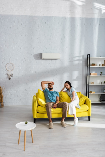 Tired couple suffering from heat on sofa in living room - Фото, изображение