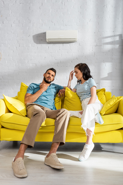 Nuori pari kärsii lämpöä ilmastointilaite seinällä taustalla olohuoneessa  - Valokuva, kuva