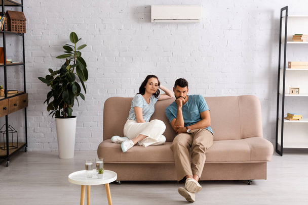 Вибірковий фокус молодої пари дивиться на камеру, сидячи на дивані у вітальні
 - Фото, зображення