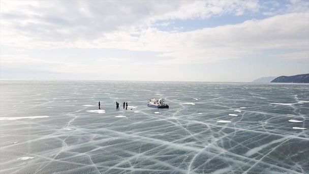 Grupo de pessoas em pé em rachaduras stnning lago de gelo perto hovercraft. Clipe. As pessoas viajam e exploram o lago Baikal congelado em um hovercraft seguro e confortável
. - Foto, Imagem