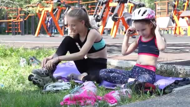 2人の女の子がローラースケートをする準備ができて、遊び場にヘルメットをかぶる。高品質のフルHD映像 - 映像、動画