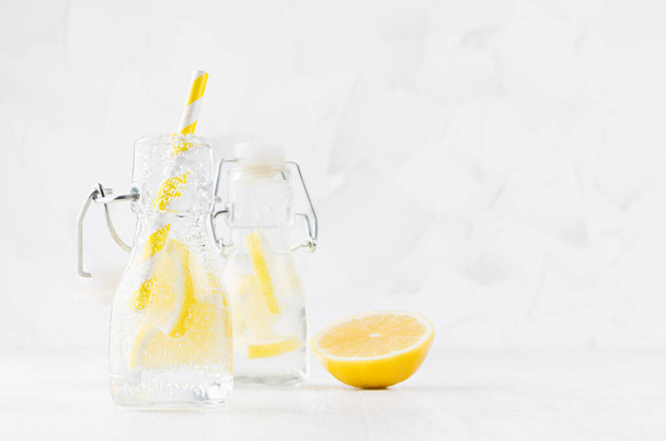 Cold fresh fruit citrus beverages of yellow lemon with soda water, bubbles, funny striped straw on simple soft bright white background, copy space. - Photo, image