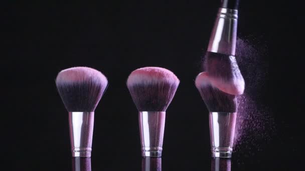 Concepto de belleza. Cepillos cosméticos con polvo cosmético rosa extendiéndose sobre fondo negro en cámara lenta
 - Imágenes, Vídeo