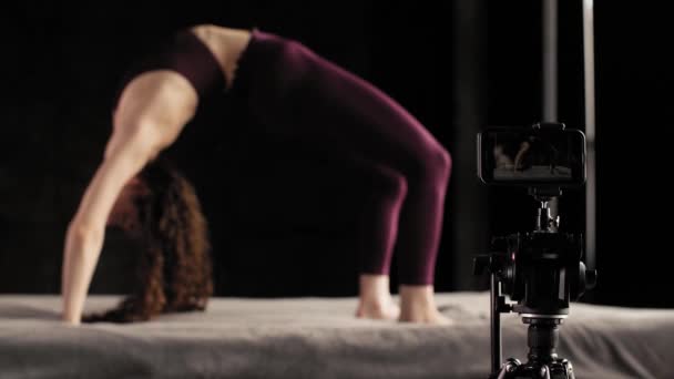 Egy jógatanár gyakorlatokat tanít egy online konferencián keresztül. A lány jógázik az ágyon, fekete alapon. - Felvétel, videó