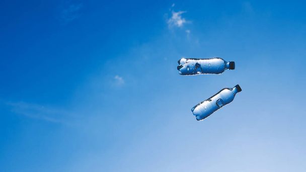 Twee vliegende flessen met water tegen de blauwe lucht op een zonnige dag. Achtergrond met kopieerruimte. Breed formaat foto. Foto van het verfrissingsconcept. - Foto, afbeelding