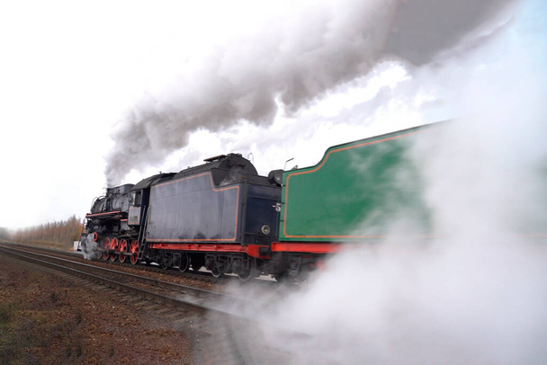 Древний локомотив ездит по железной дороге. Паровая железнодорожная машина в дыму
 - Фото, изображение