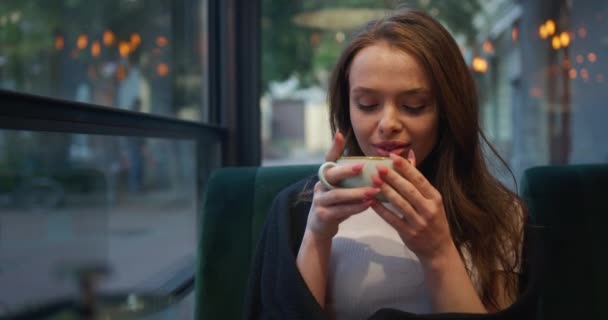 クローズアップ撮影。少女はベランダのカフェに座っている。彼女はお茶を飲んで雰囲気を楽しんでいます。少女は毛布に包まれている。4K - 映像、動画