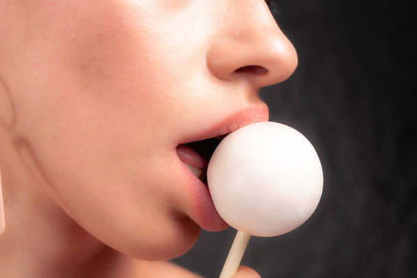 Close up of female lips and candy. Girl eating candy on a stick. Beautiful lips. - Photo, Image