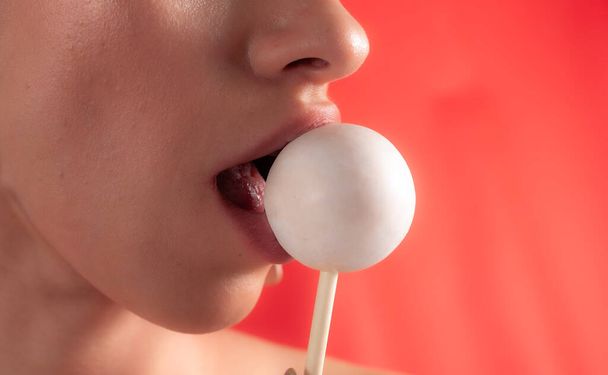 Sluiten van vrouwelijke lippen en snoep. Meisje dat snoep eet op een stokje. Mooie lippen.. - Foto, afbeelding