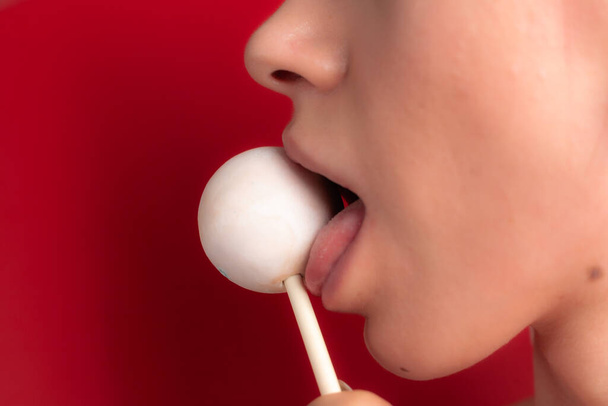 Sluiten van vrouwelijke lippen en snoep. Meisje dat snoep eet op een stokje. Mooie lippen.. - Foto, afbeelding