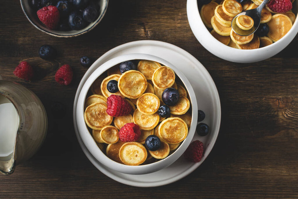 Модный домашний завтрак, блинные хлопья, мини блинчики с ягодами, вид сверху, деревянный стол
 - Фото, изображение