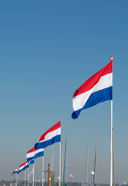 Bandeiras do Reino dos Países Baixos, bandeira nacional holandesa em três cores vermelho, branco e azul e azul céu fundo
 - Foto, Imagem