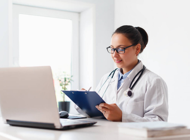 female doctor at her workplace working with laptop and clipboard - Photo, image