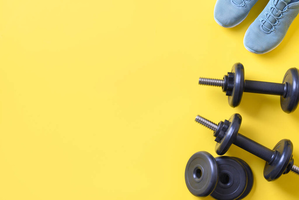Sport and fitness equipment, dumbbells, shoes on yellow. Top view, space for your text. - Foto, immagini