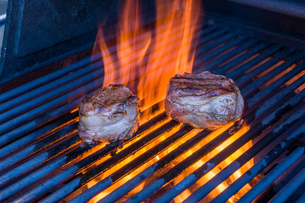 Un par de filetes mignon envueltos en tocino cocinando una parrilla con una llama
 - Foto, imagen