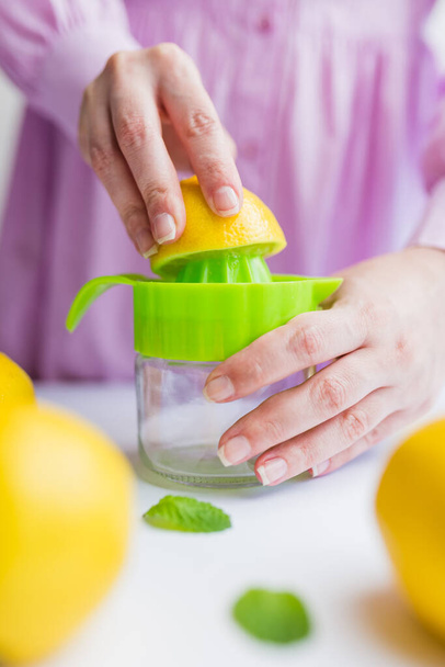 Female hands squeezing fresh lemon with plastic squeezer, healthy lifestyle concept. - Fotó, kép
