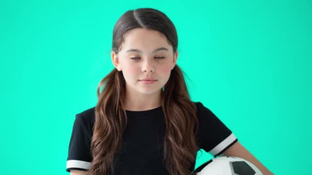 Hoofd shot portret van een schattig tienermeisje houden voetbal, kijken naar camera en lachen, staan tegen turquoise blauwe achtergrond - Video