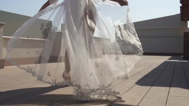 Een mooie bruid in een peignoir wandelt op het terras. Meisje in mooie lingerie, de wind blaast de jurk. - Video