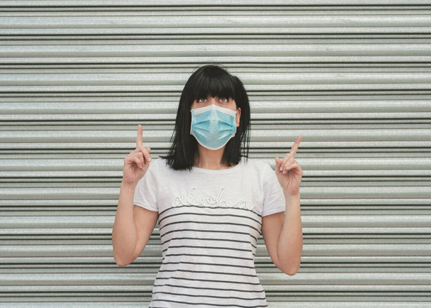 femme portant un masque médical pointage réfléchi avec deux index vers le haut et regardant au-dessus - Photo, image
