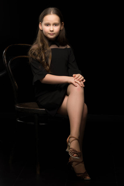 Portrait of a little girl sitting on an old Viennese chair, black background. - Фото, зображення