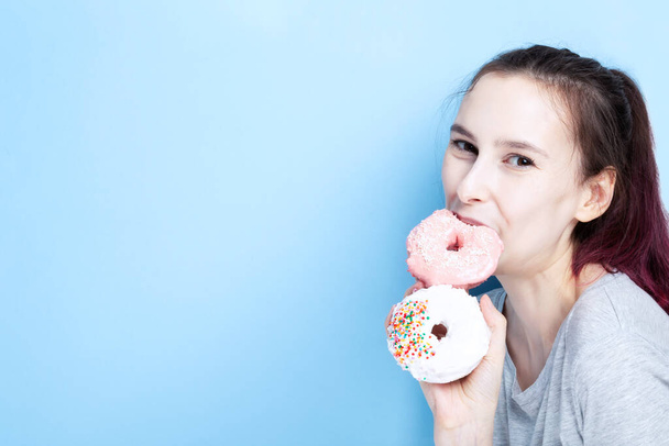 Young girl holds two donuts in her hand and bites one, blue background - Photo, Image
