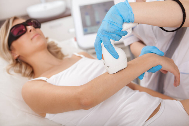 Young woman smiling while getting pailess laser hair removal on her arms at beauty clinic - Zdjęcie, obraz