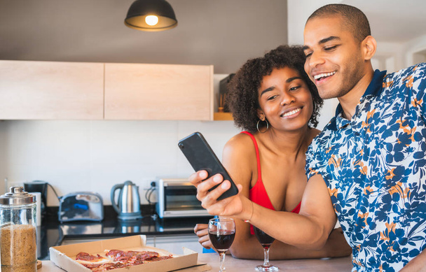 Portrait of happy young latin couple taking a selfie with mobile phone while having dinner at new home. Lifestyle and relationship concept. - Photo, image