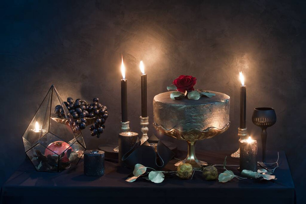 mysterious looking still life with handmade figure of cake, burning candles, dried rose and pomegranate, craft art of wedding decoration details - Фото, изображение