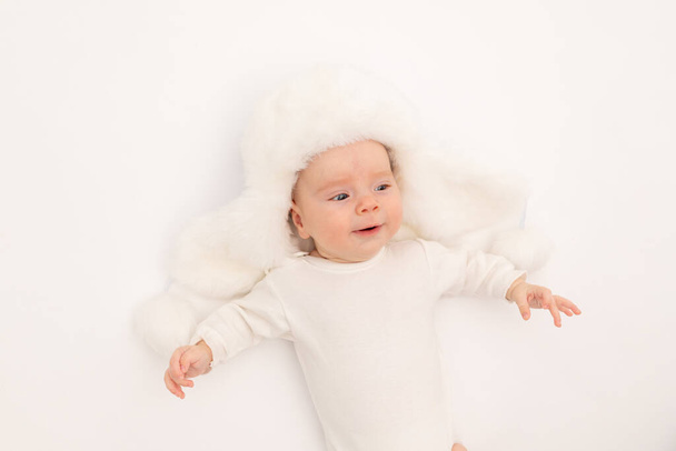 schattig baby meisje in een witte bont winter hoed op een witte geïsoleerde achtergrond, baby 3 maanden in een warme hoed, ruimte voor tekst - Foto, afbeelding