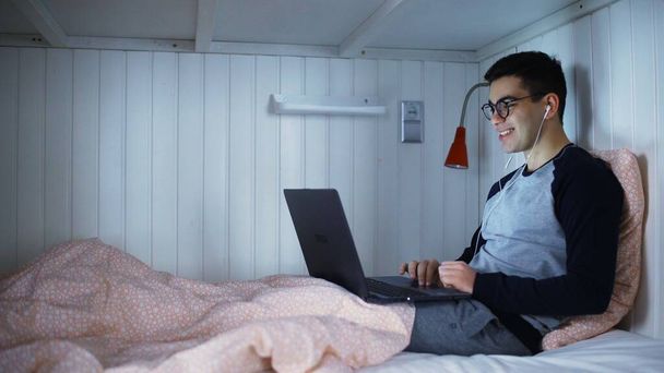Man lying in a bed and talking on a web camera and smiling - Foto, immagini