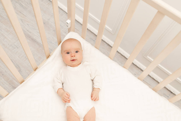 Το κοιμισμένο μωρό και το παιχνίδι του σε άσπρη κούνια. Βρεφοκομείο και κρεβάτια για παιδιά. Χαριτωμένο αγοράκι που κοιμάται στην κούνια. Το παιδί παίρνει έναν υπνάκο στο λευκό υπνοδωμάτιο. Υγιές παιδί με πιτζάμες.. - Φωτογραφία, εικόνα