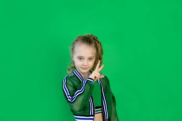 カールした髪の明るい女の子がカメラを見て2本の指を見せ緑の背景に立っている。テキストの空間 - 写真・画像