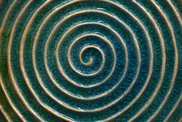 The ceramic image of a spiral with light rounds against the background of blue glaze. - 写真・画像