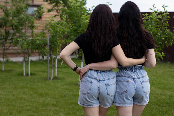 Dos mujeres morenas jóvenes con una camiseta negra y pantalones cortos de mezclilla abrazándose. Hermanas, novias.familia y concepto de amistad
 - Foto, Imagen
