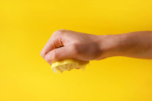 A kéz összezúzza a friss citromot. A gyümölcslevet letörölték egy citromról. Savanyú. - Fotó, kép