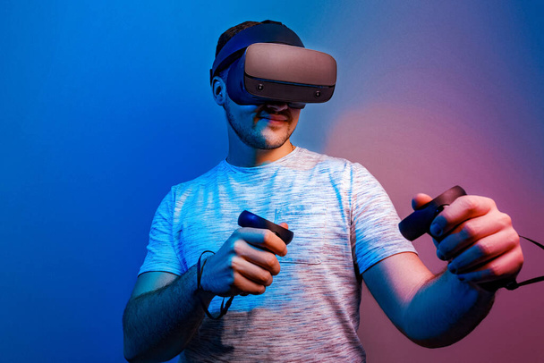 Emotionaalinen nuori mies virtuaalitodellisuus lasit studiossa sininen valo - Valokuva, kuva